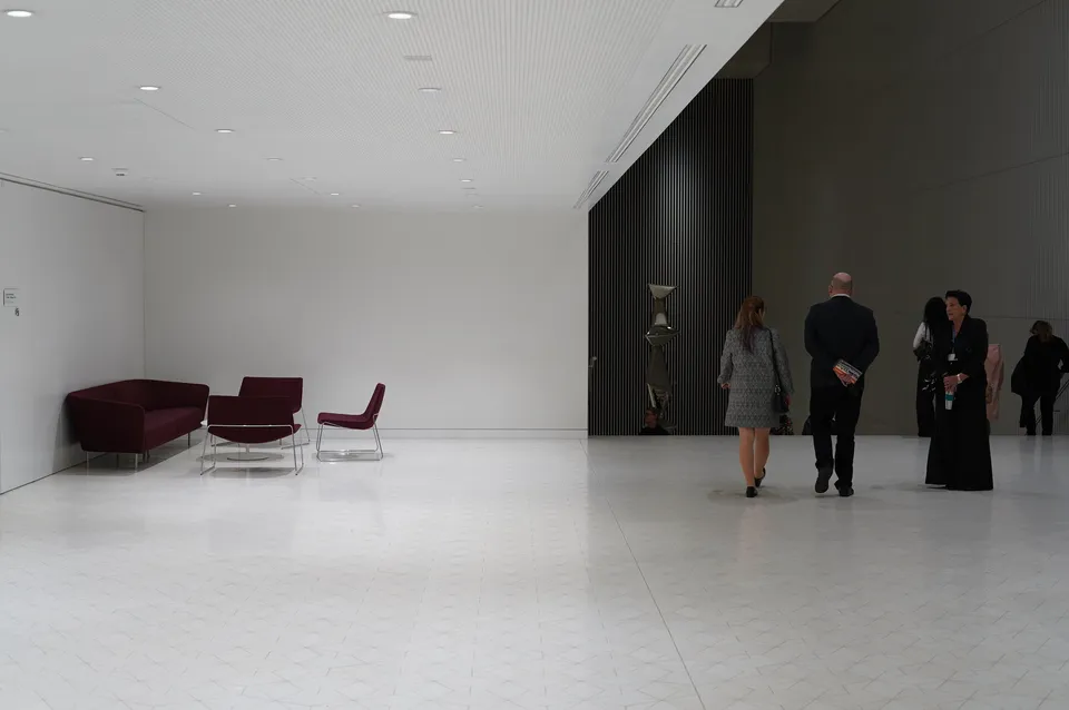 Weißer Innenraum mit dunkler Lamellenwand, Besucher gehen durch den leeren Raum
