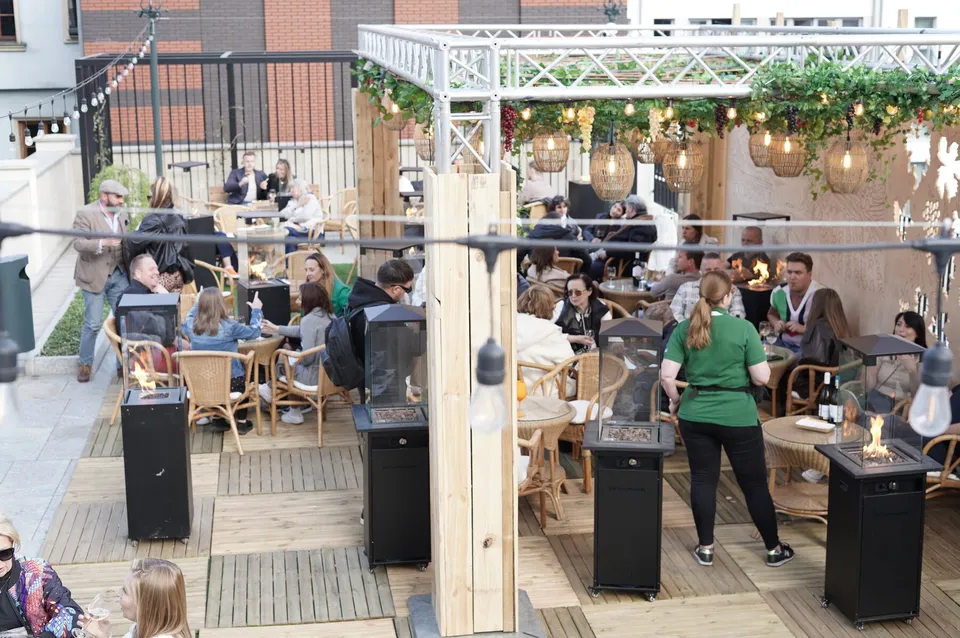 Gastgarten mit Lichterketten und Holztischen, Gäste an den Tischen